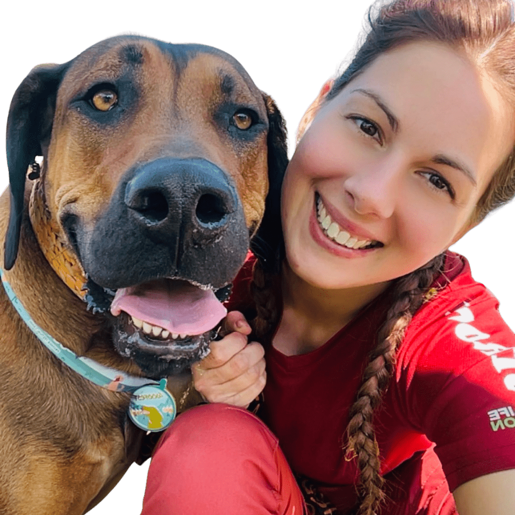 L'image montre une femme souriante qui profite de la nature avec son chien. La scène capture un moment de joie entre la personne et son animal de compagnie, mettant en valeur leur lien dans un cadre naturel.